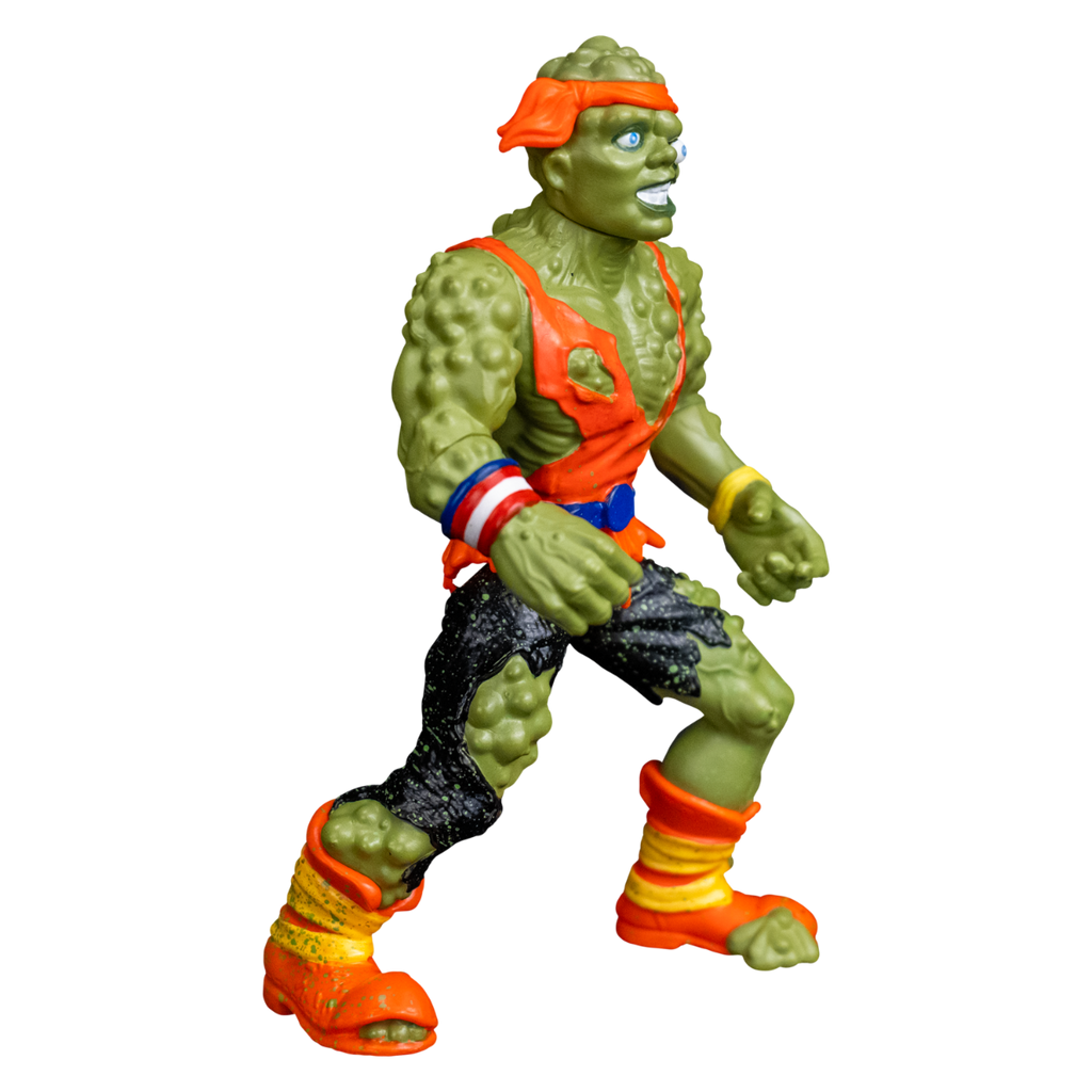 Toxie action figure, right view. Green, lumpy, muscular humanoid figure. Bald, green lumpy blistered flesh, with bright orange headband tied around forehead. Misaligned blue eyes, crooked nose. Lips open showing large teeth. Wearing tattered orange tank top, blue belt, tattered black pants, orange and yellow battered boots. red white and blue wrist band on right wrist, yellow wristband on left wrist.