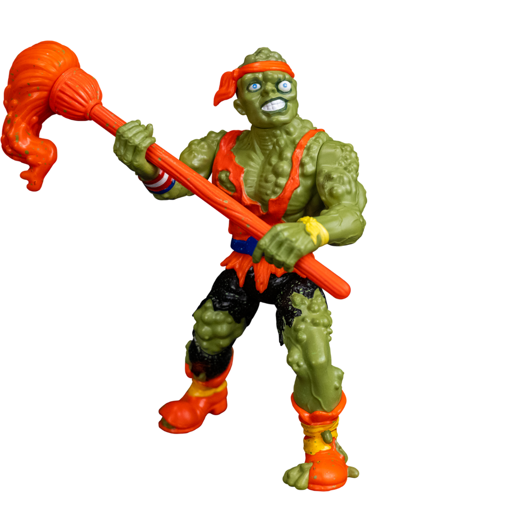 Toxie action figure, front view. Green, lumpy, muscular humanoid figure. Bald, green lumpy blistered flesh, with bright orange headband tied around forehead. Misaligned blue eyes, crooked nose. Lips open showing large teeth. Wearing tattered orange tank top, blue belt, tattered black pants, orange and yellow battered boots. red white and blue wrist band on right wrist, yellow wristband on left wrist. Holding orange mop accessory in both hands.