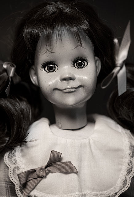 Closeup view, Black and white, Talky Tina doll head and shoulders, hair in two ponytails with bows. pointed eyebrows, large eyes slight smile.  .